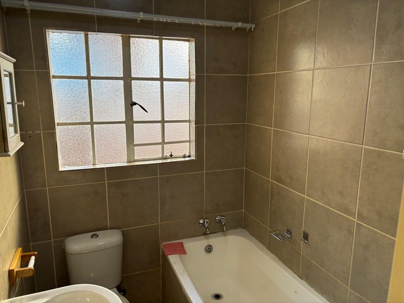A functional bathroom featuring a bathtub, toilet, and basin with neutral wall tiling and a window providing natural light.