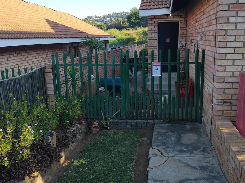 A rear exterior view showing a face brick house facade, a concrete walkway with visible cracking, and a green metal security gate.