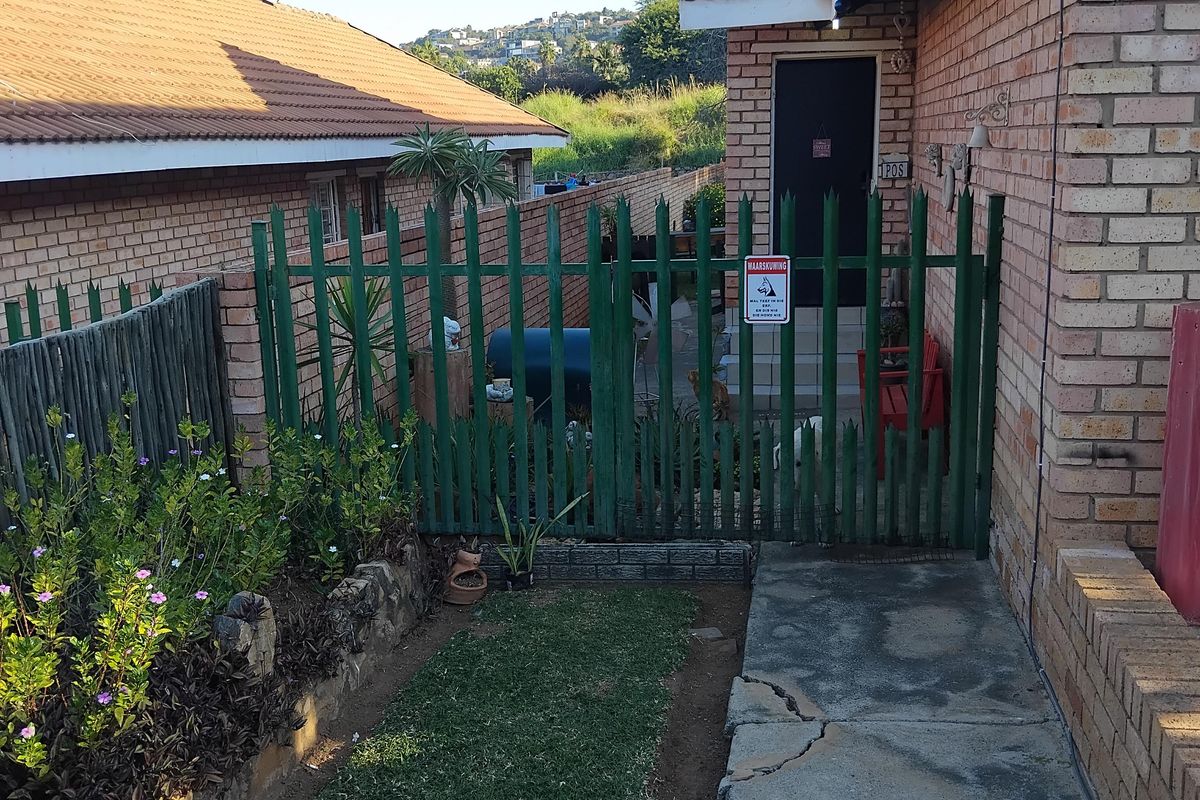 A rear exterior view showing a face brick house facade, a concrete walkway with visible cracking, and a green metal security gate.