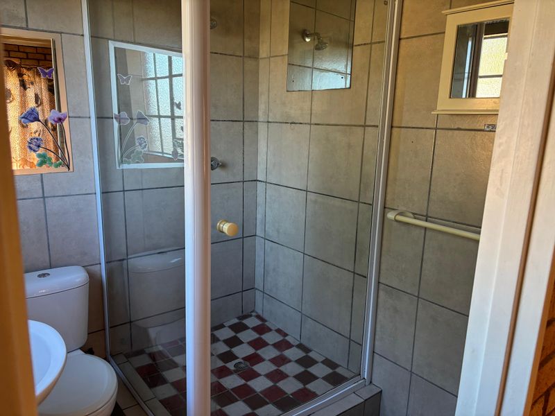A functional bathroom featuring a shower enclosure, pedestal basin, and toilet with dated wall and floor tiling.