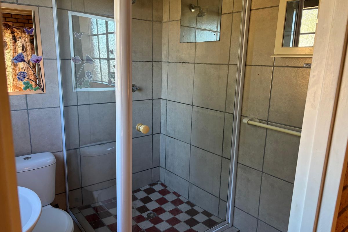 A functional bathroom featuring a shower enclosure, pedestal basin, and toilet with dated wall and floor tiling.