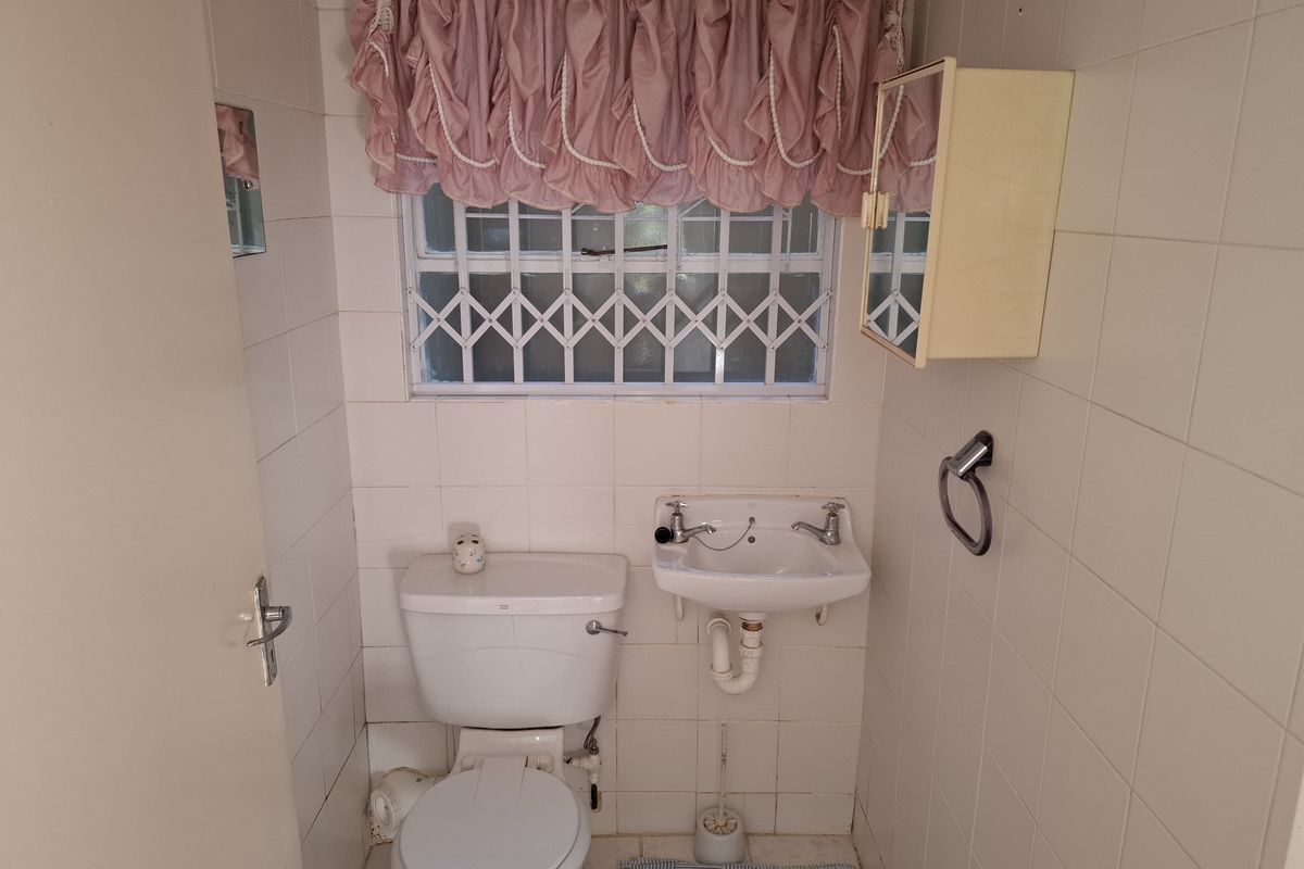 A compact guest bathroom featuring white wall tiles, a standard toilet, and a wall-mounted basin with security bars on the window.