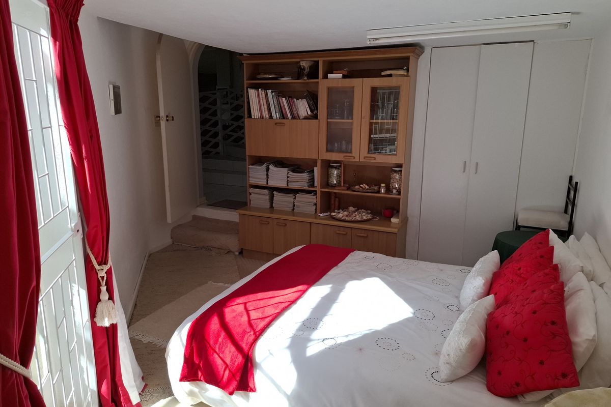 A bedroom featuring built-in storage cupboards and a wooden shelving unit, with access to an adjacent hallway area.