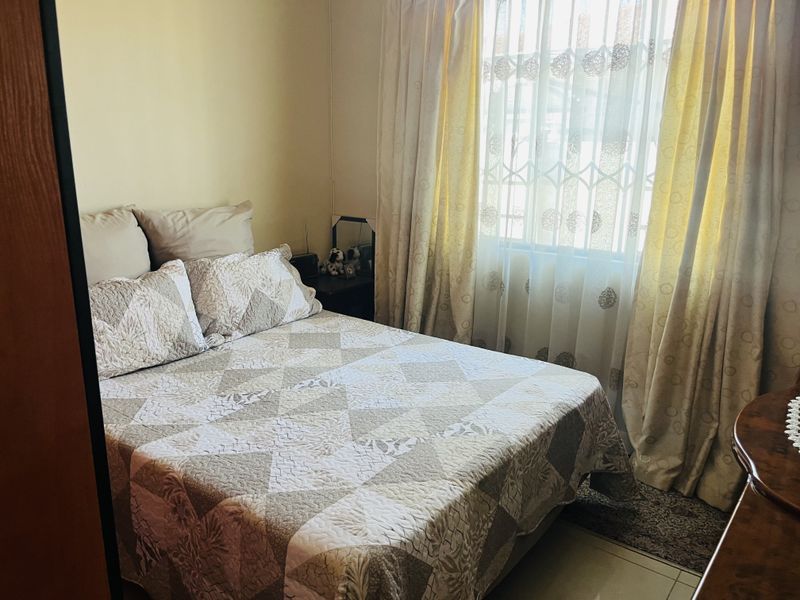A functional bedroom featuring tiled flooring and a window fitted with a security gate, providing natural light and basic security.