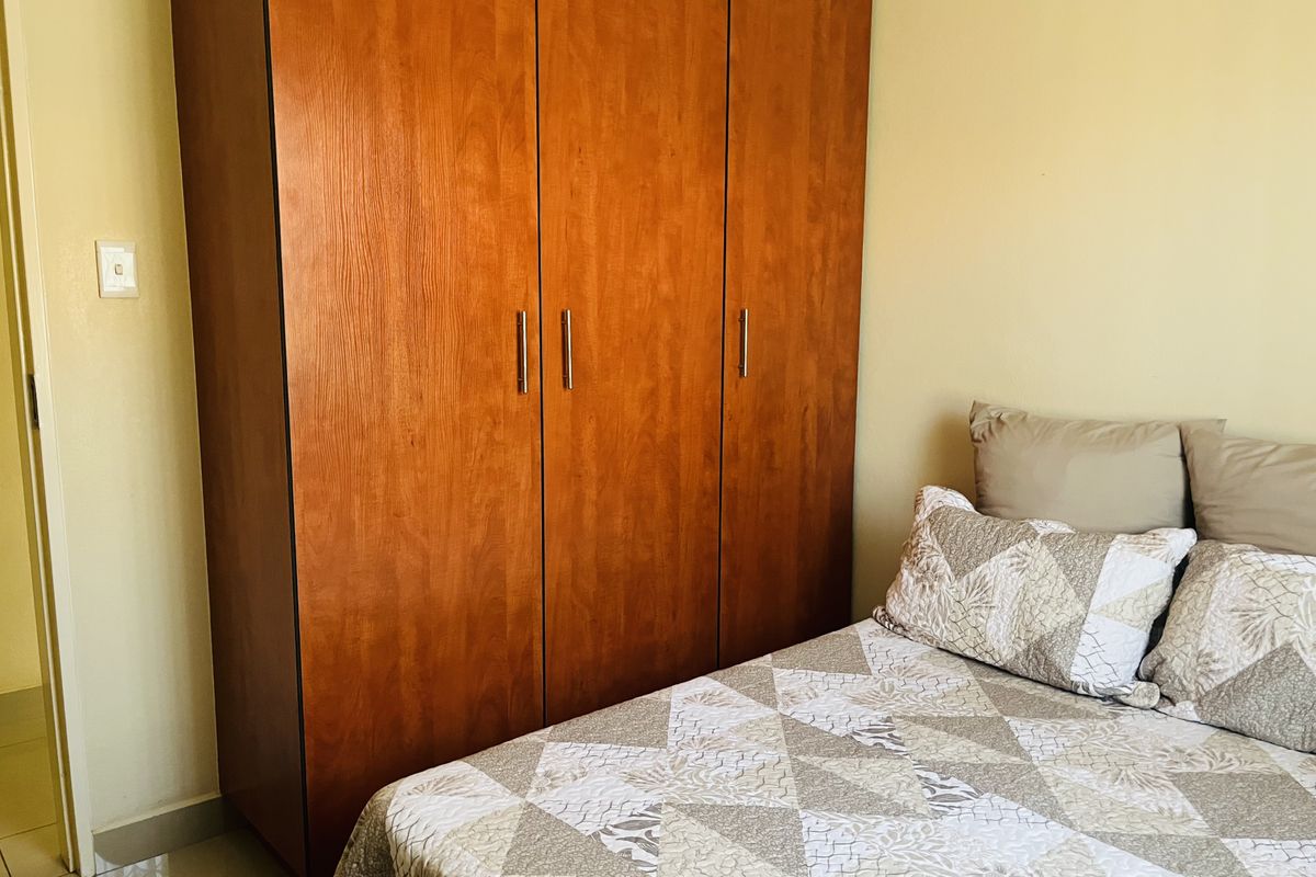A bedroom featuring a large wooden built-in wardrobe and neutral tiled flooring.
