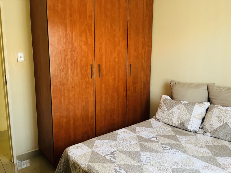 A bedroom featuring a large wooden built-in wardrobe and neutral tiled flooring.