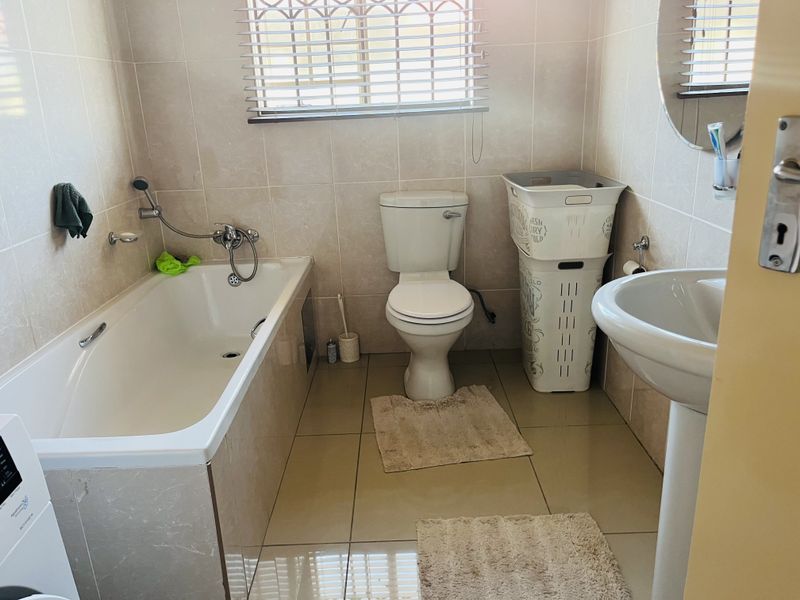 A functional bathroom featuring a bathtub, pedestal basin, and toilet with neutral wall and floor tiling.