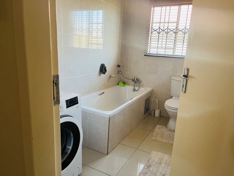 A functional bathroom featuring a bathtub, toilet, and tiled finishes, with a window providing natural light.