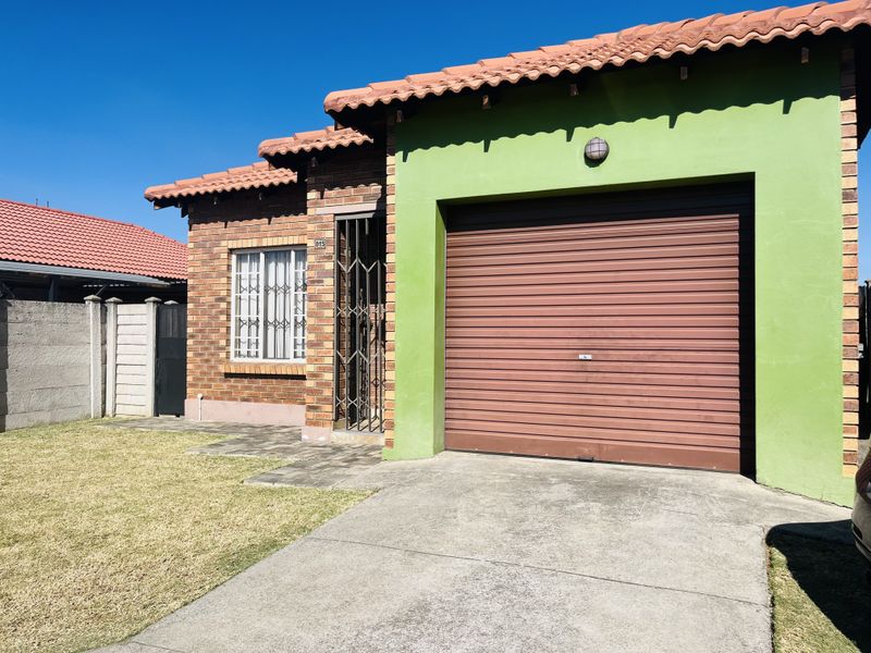 Front elevation of a townhouse featuring a brick facade, a single roller shutter garage, and a paved driveway with a small front lawn.