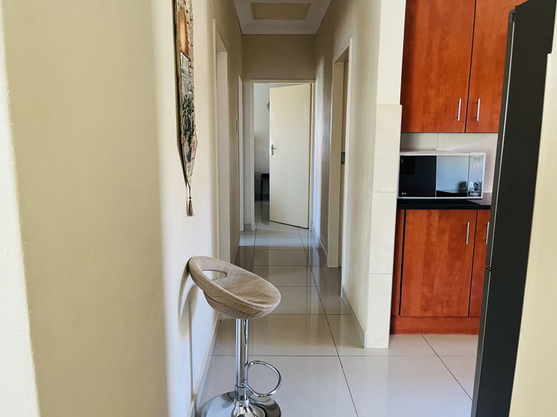 A view of a tiled hallway leading to interior rooms, featuring adjacent kitchen cabinetry with wood-finish cupboards and dark countertops.