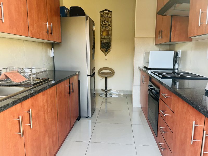 A functional galley-style kitchen featuring granite countertops, built-in oven, electric hob, extractor fan, and ample laminate cabinetry with tiled flooring.