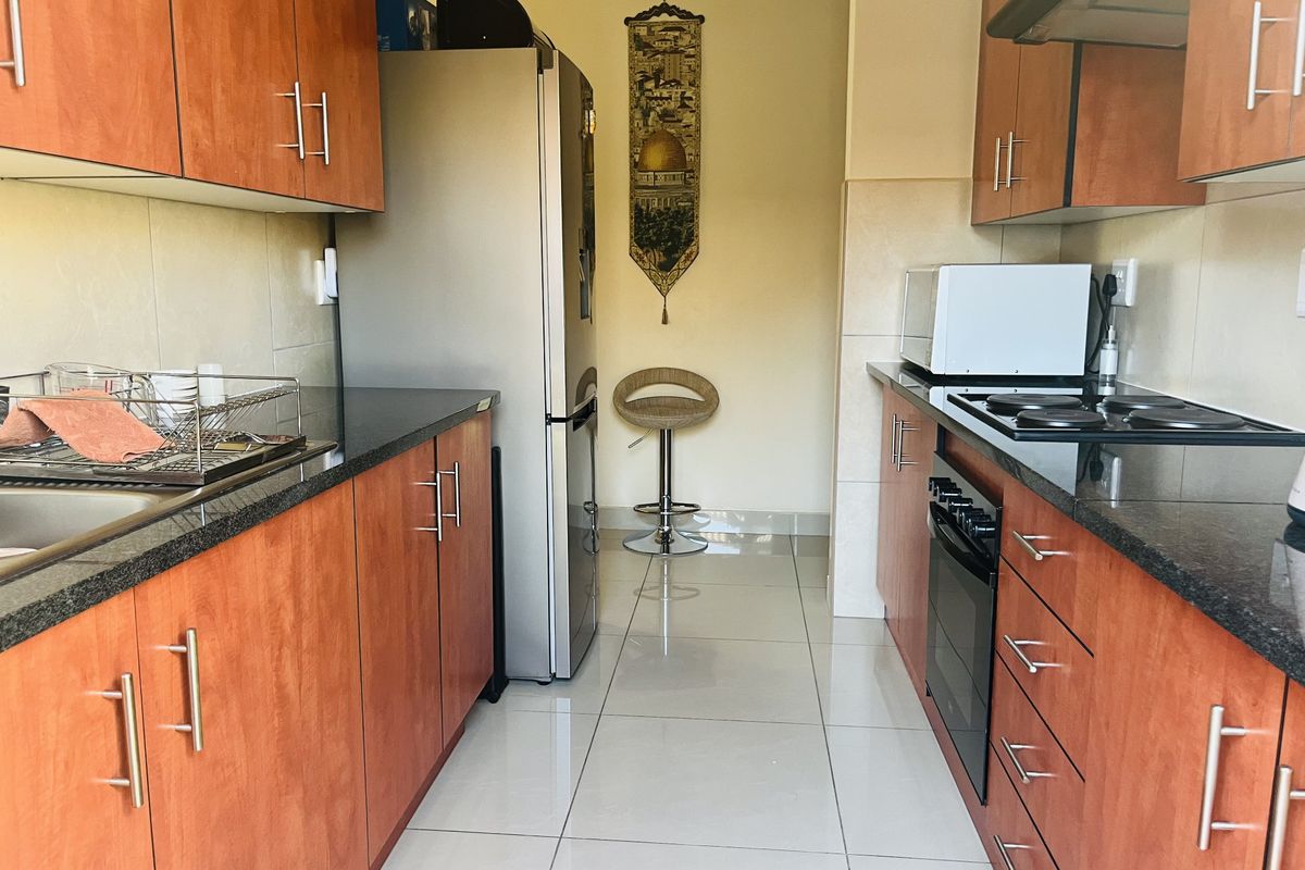A functional galley-style kitchen featuring granite countertops, built-in oven, electric hob, extractor fan, and ample laminate cabinetry with tiled flooring.