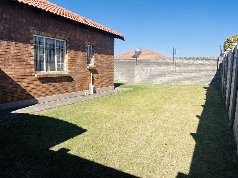 A private rear garden featuring a face brick townhouse exterior, paved walkway, and secure perimeter walling with electric fencing.