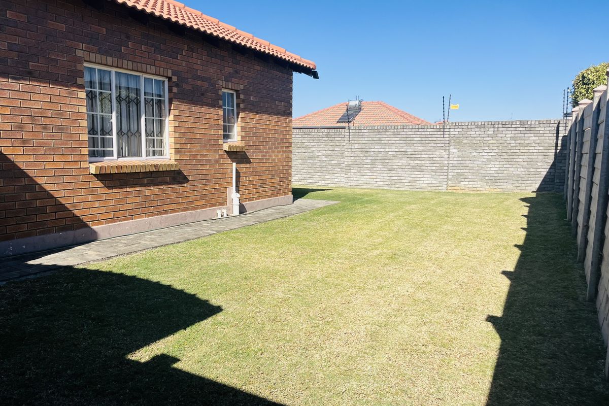 A private rear garden featuring a face brick townhouse exterior, paved walkway, and secure perimeter walling with electric fencing.