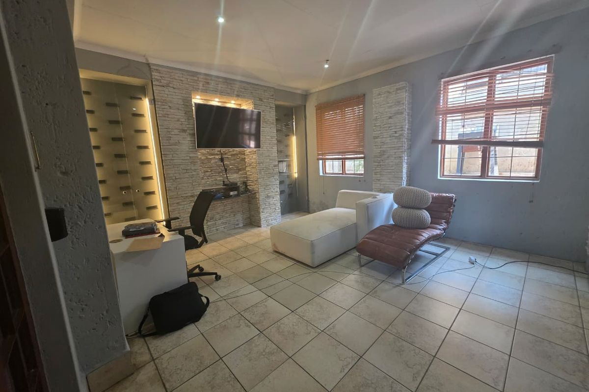 A versatile living space featuring stone-clad feature walls, recessed lighting, tiled flooring, and integrated glass-panelled storage units.