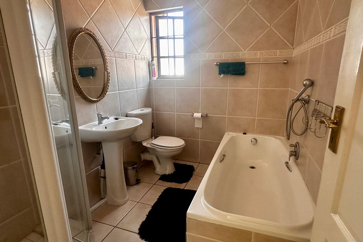 A functional bathroom featuring a pedestal basin, a built-in bathtub, a separate shower enclosure, and tiled walls with a decorative border.