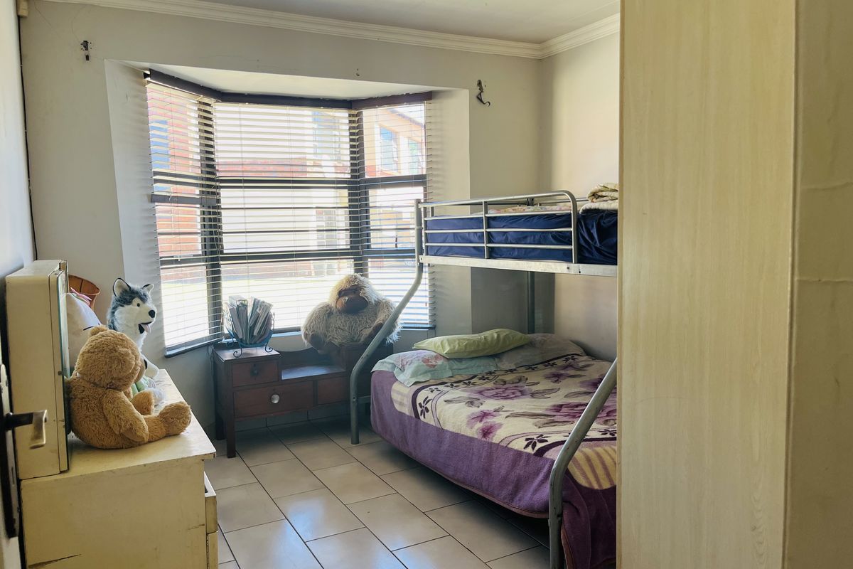 A bedroom featuring tiled flooring and a bay window with fitted blinds, offering natural light and a functional layout.