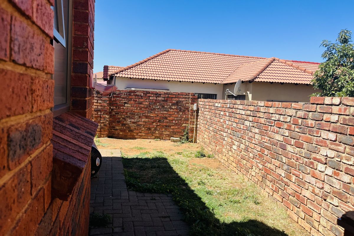 A private rear courtyard featuring brick boundary walls, paved walkway, and a small garden area, offering potential for landscaping and outdoor living.