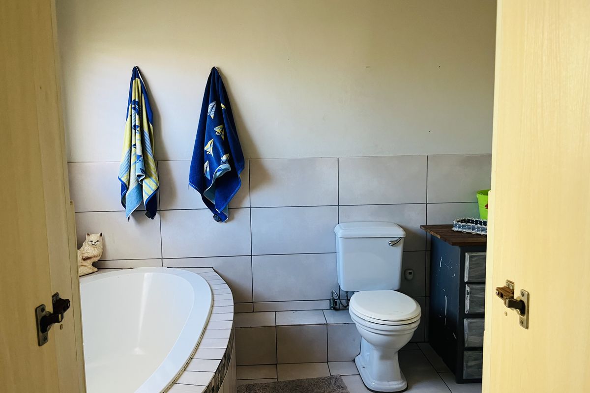 A functional bathroom featuring a built-in bathtub with tiled surround and a standard toilet, finished with neutral wall tiles.