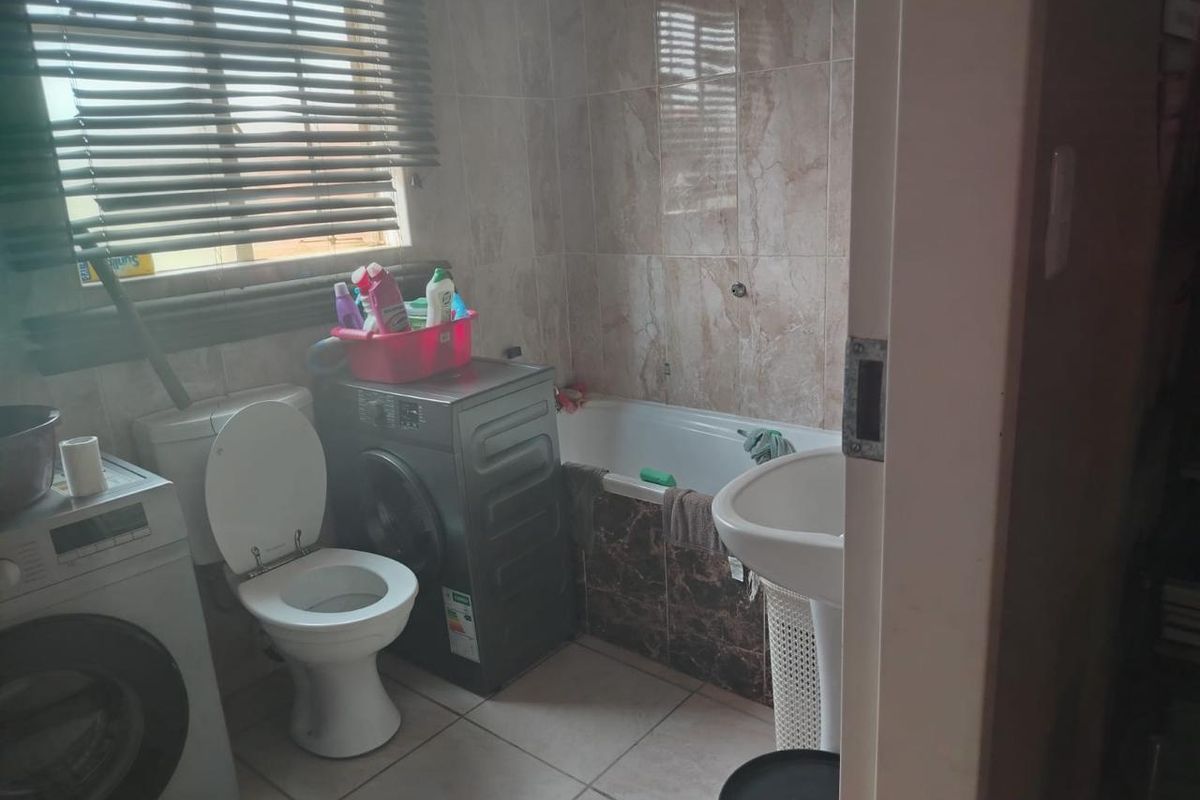 A functional bathroom featuring a pedestal basin, toilet, and a bathtub with tiled surround, including space for laundry appliances.