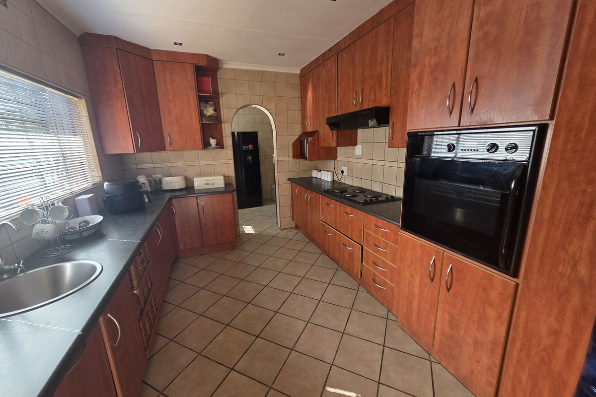 A functional kitchen featuring wood-finish cabinetry, dark countertops, a built-in oven, and a hob with an extractor fan, leading to an adjacent utility area.