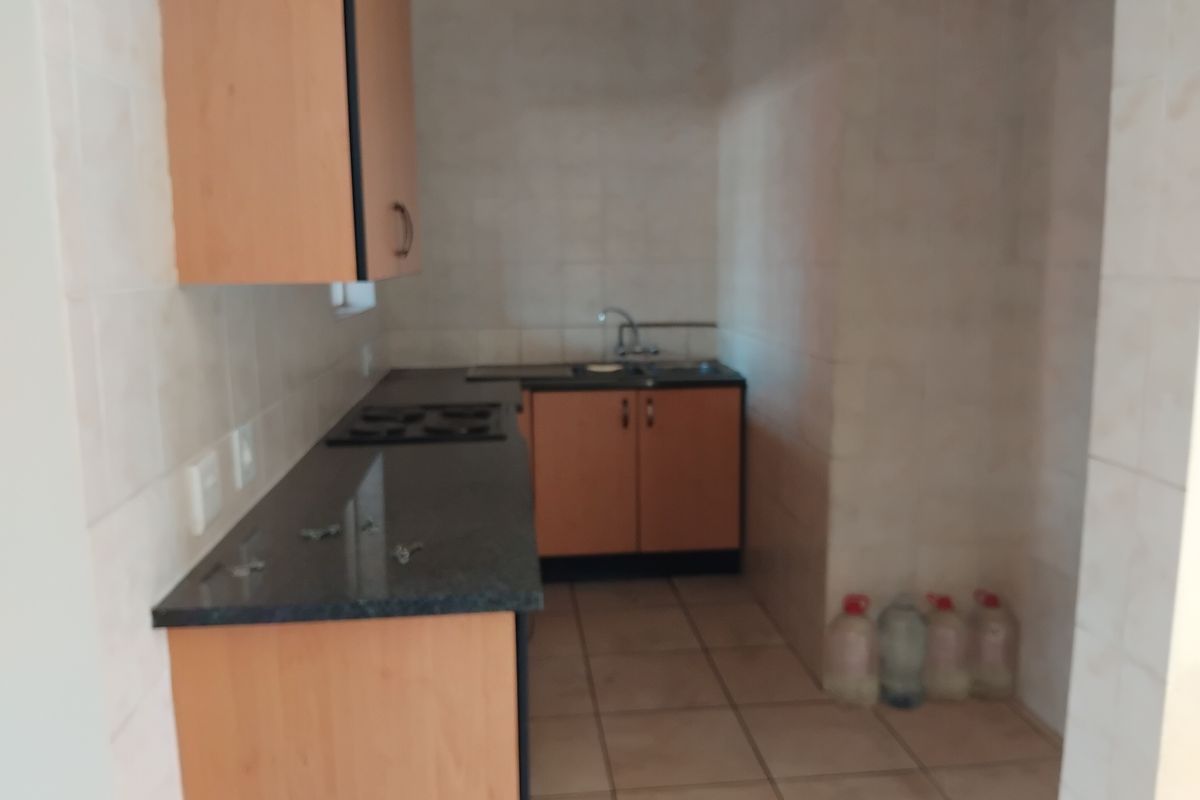 A compact kitchen featuring built-in wooden cabinetry, granite countertops, a built-in hob, and a stainless steel sink with tiled finishes throughout.