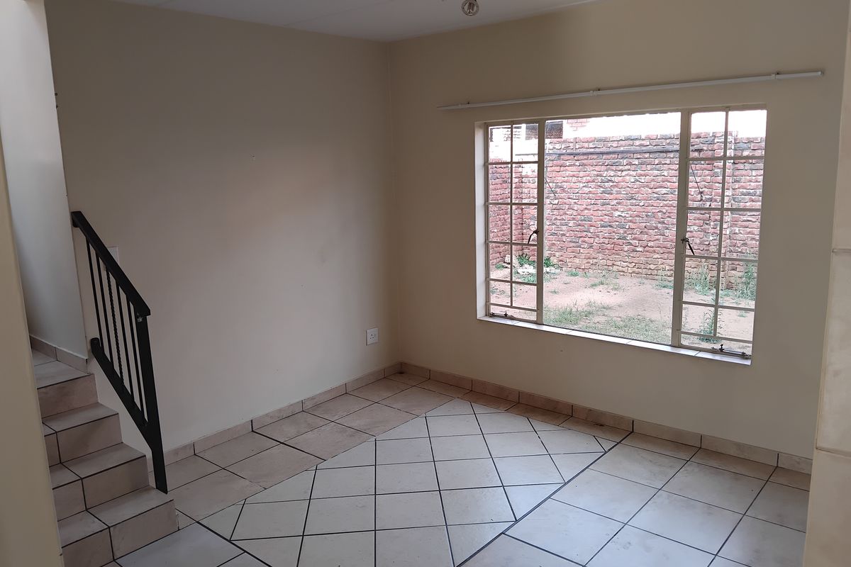 An empty living room featuring tiled flooring, a staircase with a metal railing, and a large window overlooking the rear exterior area.