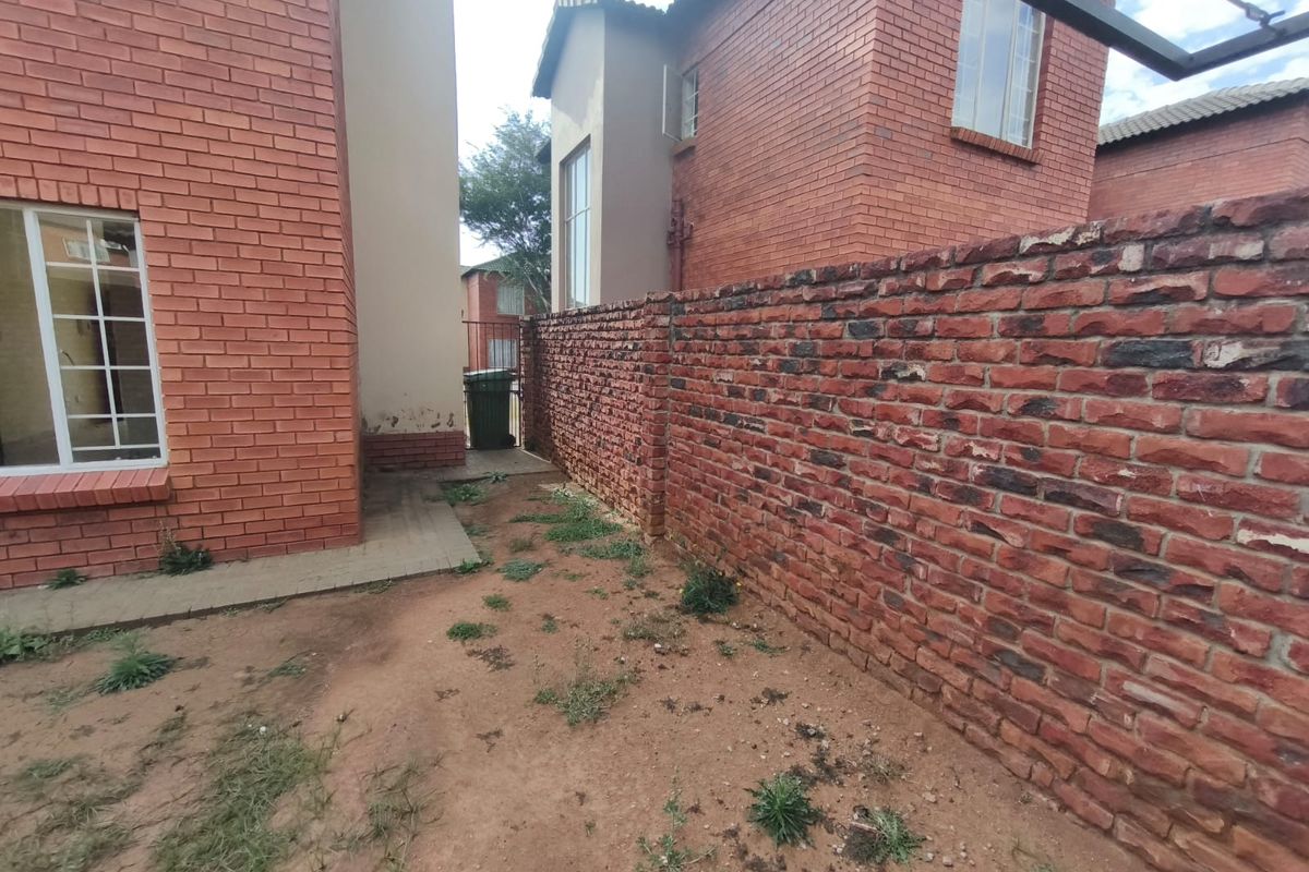 Rear exterior view of the apartment featuring face brick walls, a boundary wall, and an unlandscaped garden area.