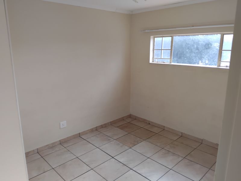 An empty bedroom featuring tiled flooring, a window with a curtain rail, and neutral wall paint, ready for personalization.