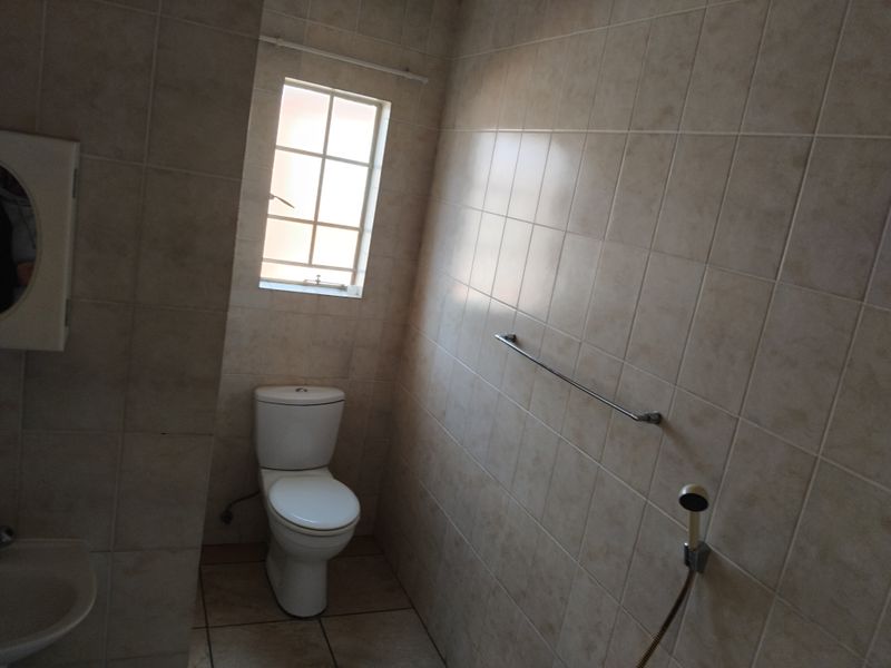 A functional bathroom featuring floor-to-ceiling tiling, a standard toilet, and a handheld shower attachment.