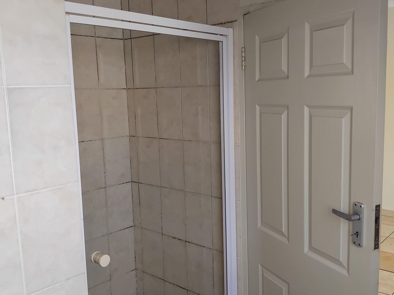 A compact bathroom featuring a shower enclosure with tiled walls and flooring, requiring cosmetic updates to the grout and ceiling finish.