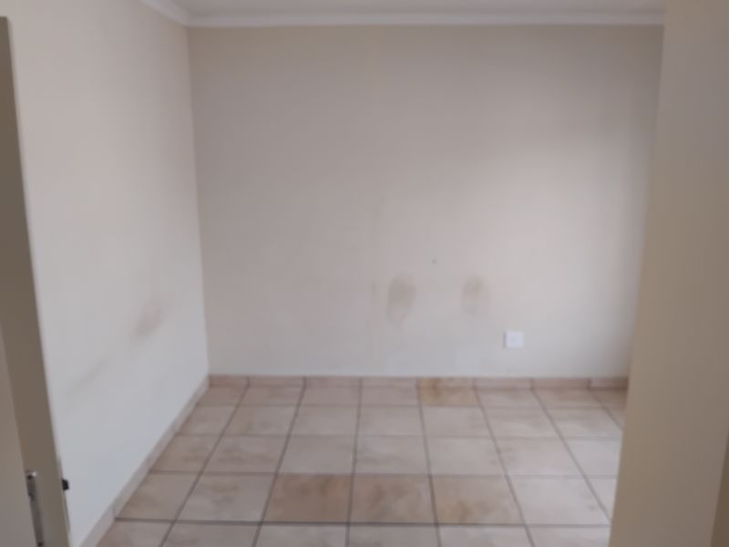 An empty bedroom featuring tiled flooring and plain walls, currently showing signs of wear and staining requiring cosmetic attention.