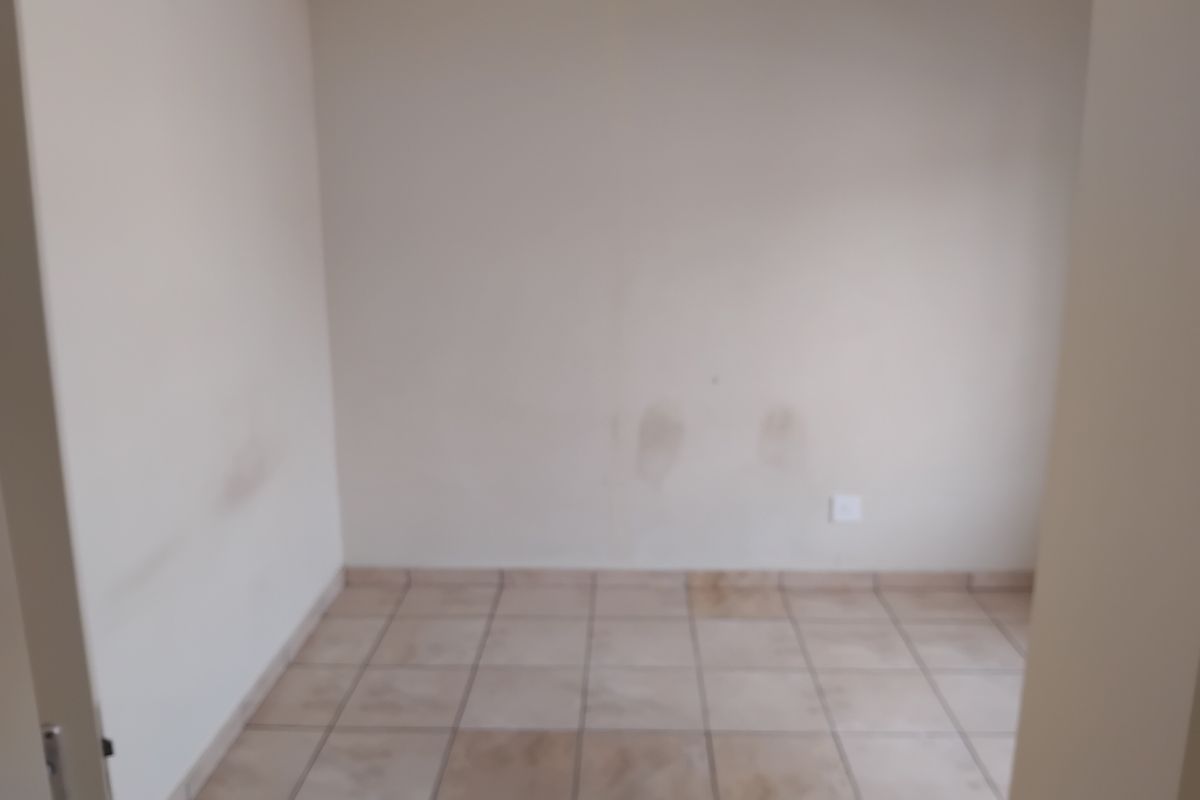 An empty bedroom featuring tiled flooring and plain walls, currently showing signs of wear and staining requiring cosmetic attention.