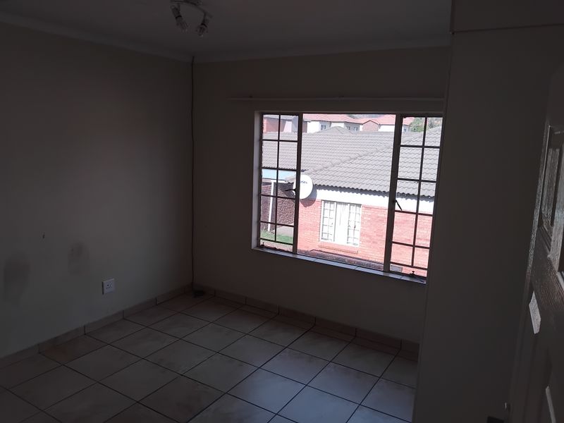 An empty bedroom featuring tiled flooring and a large grid-pattern window, providing a neutral space ready for personalization.