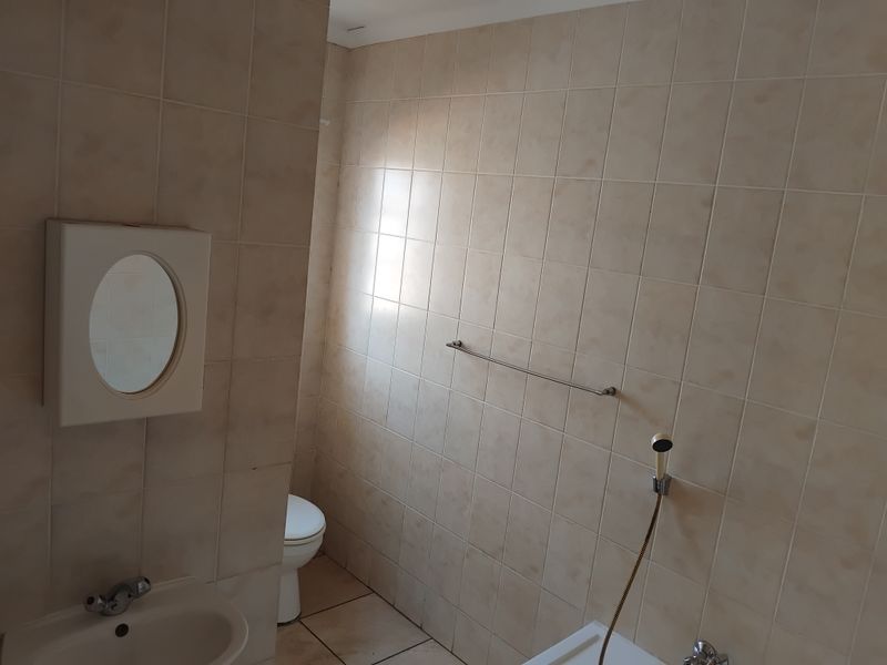A functional bathroom featuring ceramic wall tiles, a wall-mounted basin, toilet, and shower fixture, offering a blank canvas for modern renovation.
