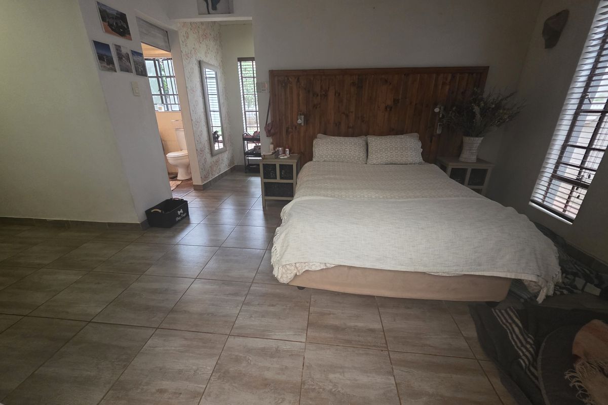 Spacious bedroom featuring tiled flooring, a built-in wooden headboard, and an adjoining en-suite bathroom with natural light through venetian blinds.