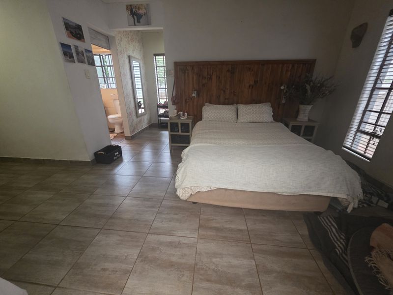 Spacious bedroom featuring tiled flooring, a built-in wooden headboard, and an adjoining en-suite bathroom with natural light through venetian blinds.