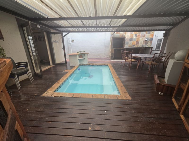 Covered outdoor entertainment area featuring a swimming pool, timber decking, and a built-in braai station, ideal for relaxed alfresco dining and leisure.