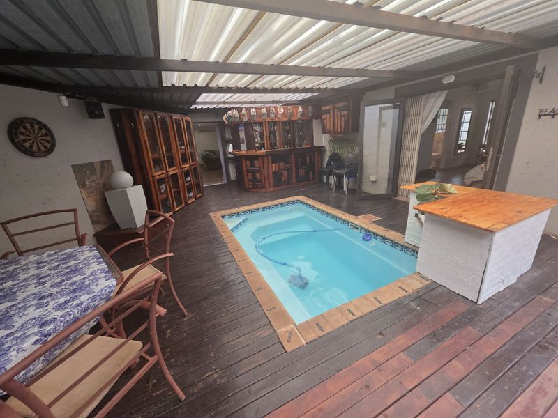 Covered outdoor entertainment area featuring a built-in bar, timber decking, and a central swimming pool.
