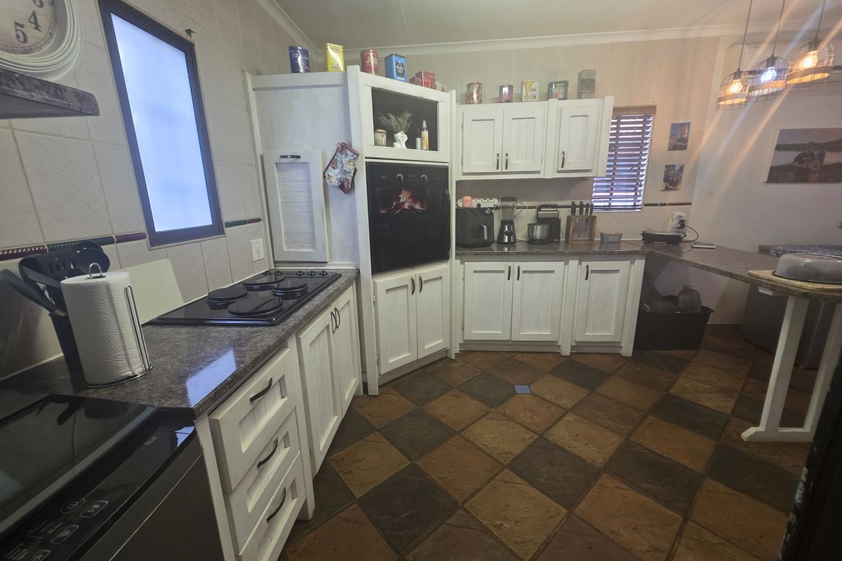 A functional kitchen featuring white cabinetry, granite countertops, a built-in oven, electric hob, and a breakfast bar area with tiled flooring.