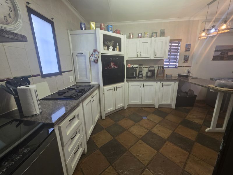 A functional kitchen featuring white cabinetry, granite countertops, a built-in oven, electric hob, and a breakfast bar area with tiled flooring.