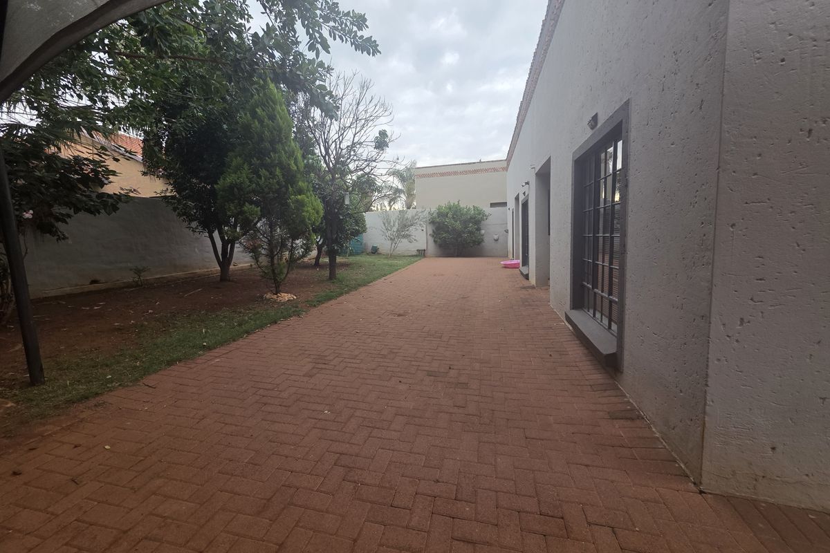 A spacious rear exterior area featuring a paved patio, perimeter wall, and established garden trees.