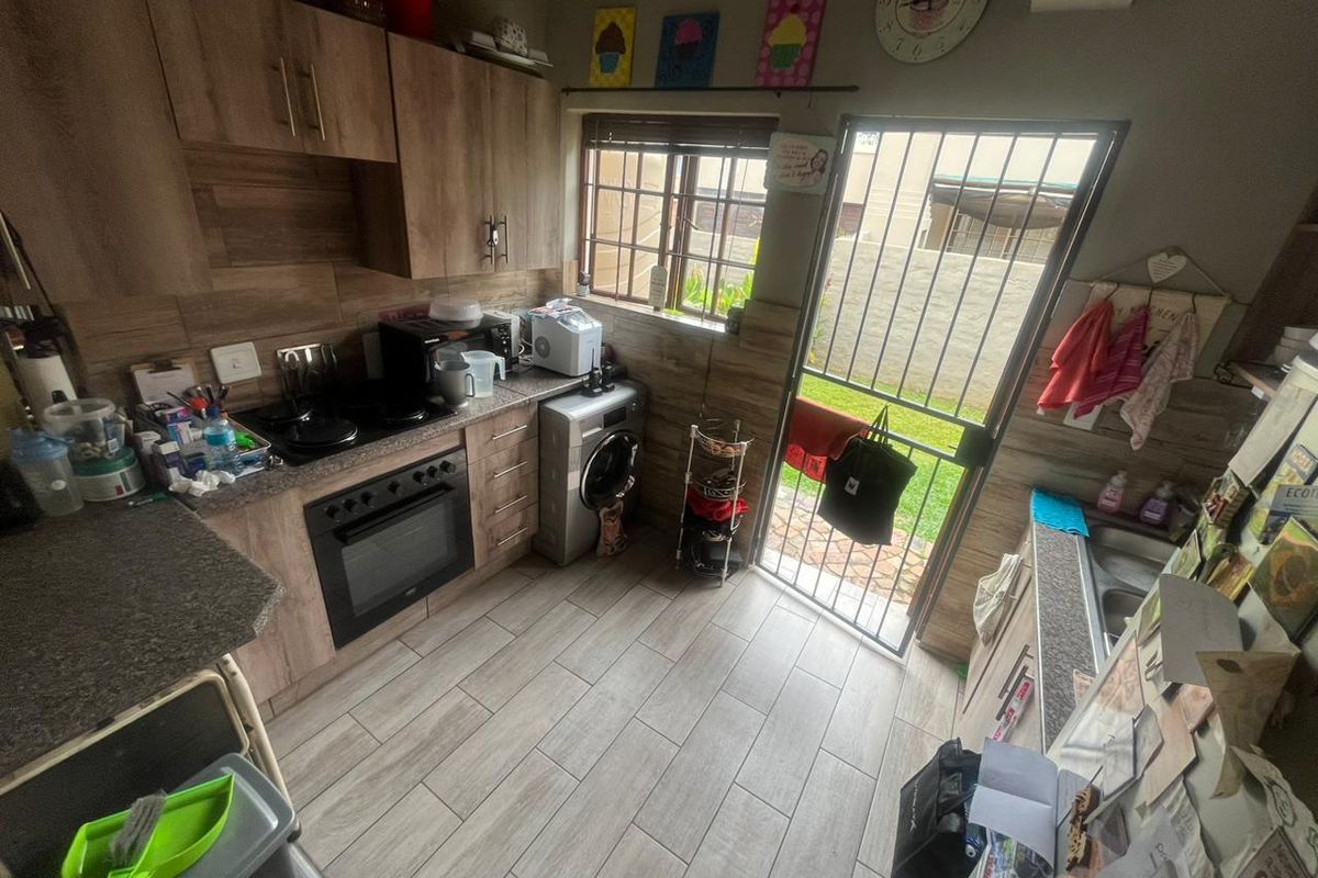 A functional kitchen featuring wood-look cabinetry, tiled flooring, a built-in oven and hob, and direct access to the rear garden through a security gate.