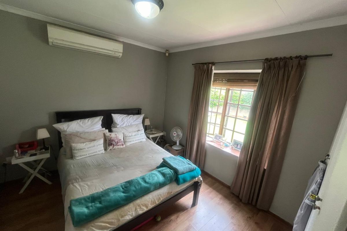 A cozy bedroom featuring laminate flooring, a wall-mounted air conditioning unit, and a window with natural light.