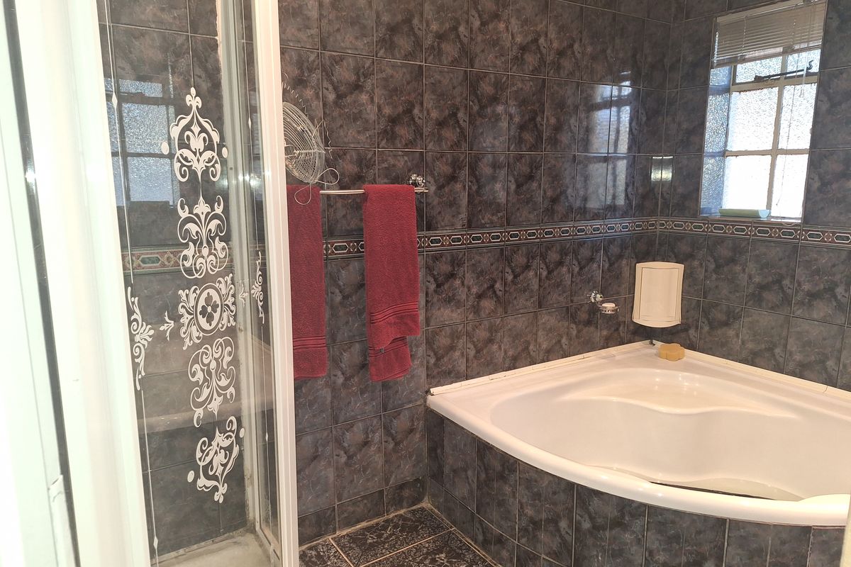 A bathroom featuring a corner bathtub and a separate shower enclosure with dark patterned wall and floor tiles.