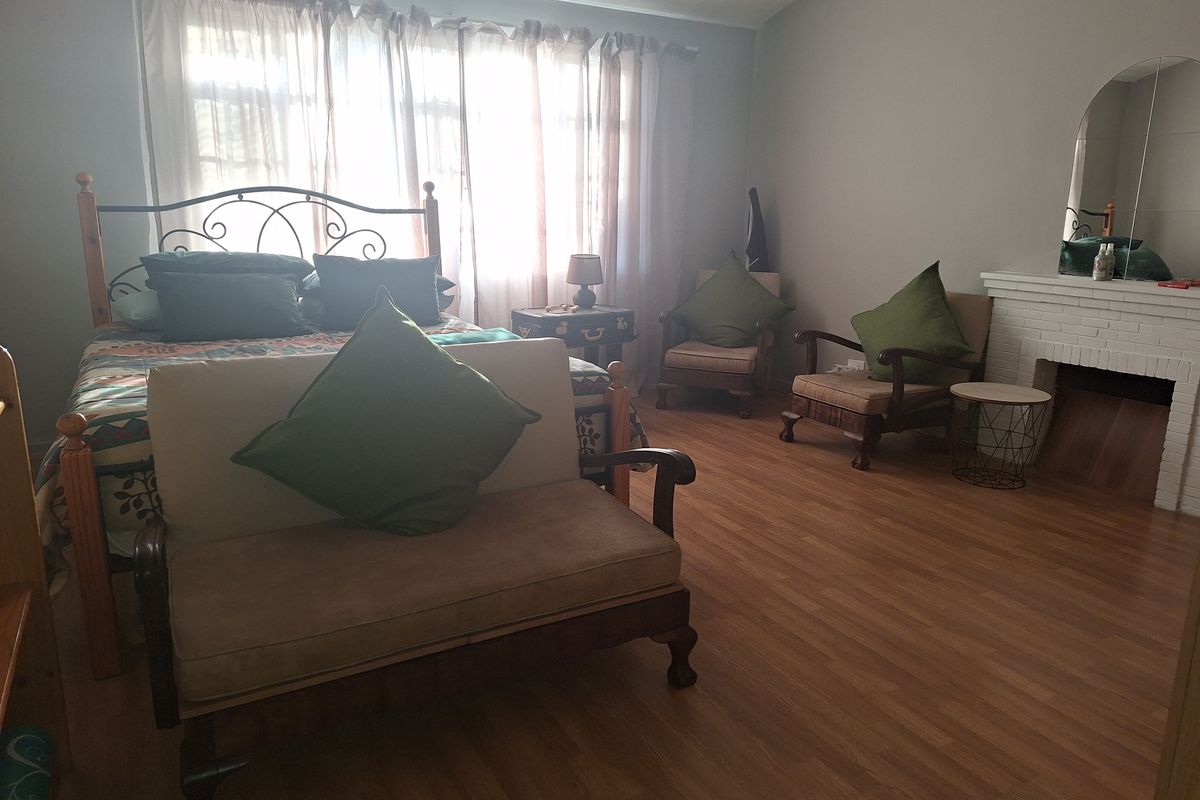 Spacious bedroom featuring wood-look laminate flooring, a white painted brick fireplace, and large windows allowing for ample natural light.
