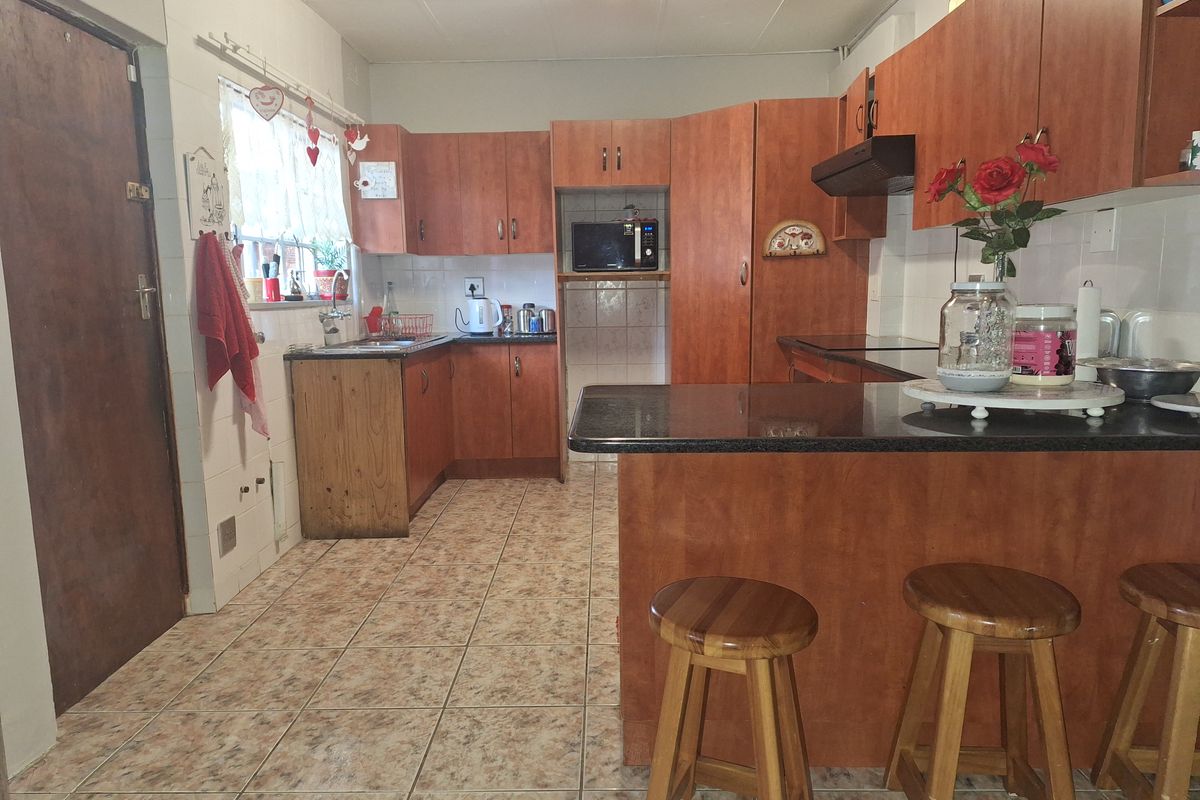 A functional kitchen featuring wood-look cabinetry, dark granite countertops, a breakfast bar, and tiled flooring with a built-in extractor fan.