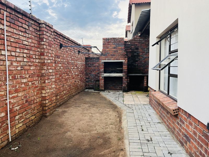 Rear courtyard area featuring a built-in brick braai, paved walkway, and high boundary walls with electric fencing.