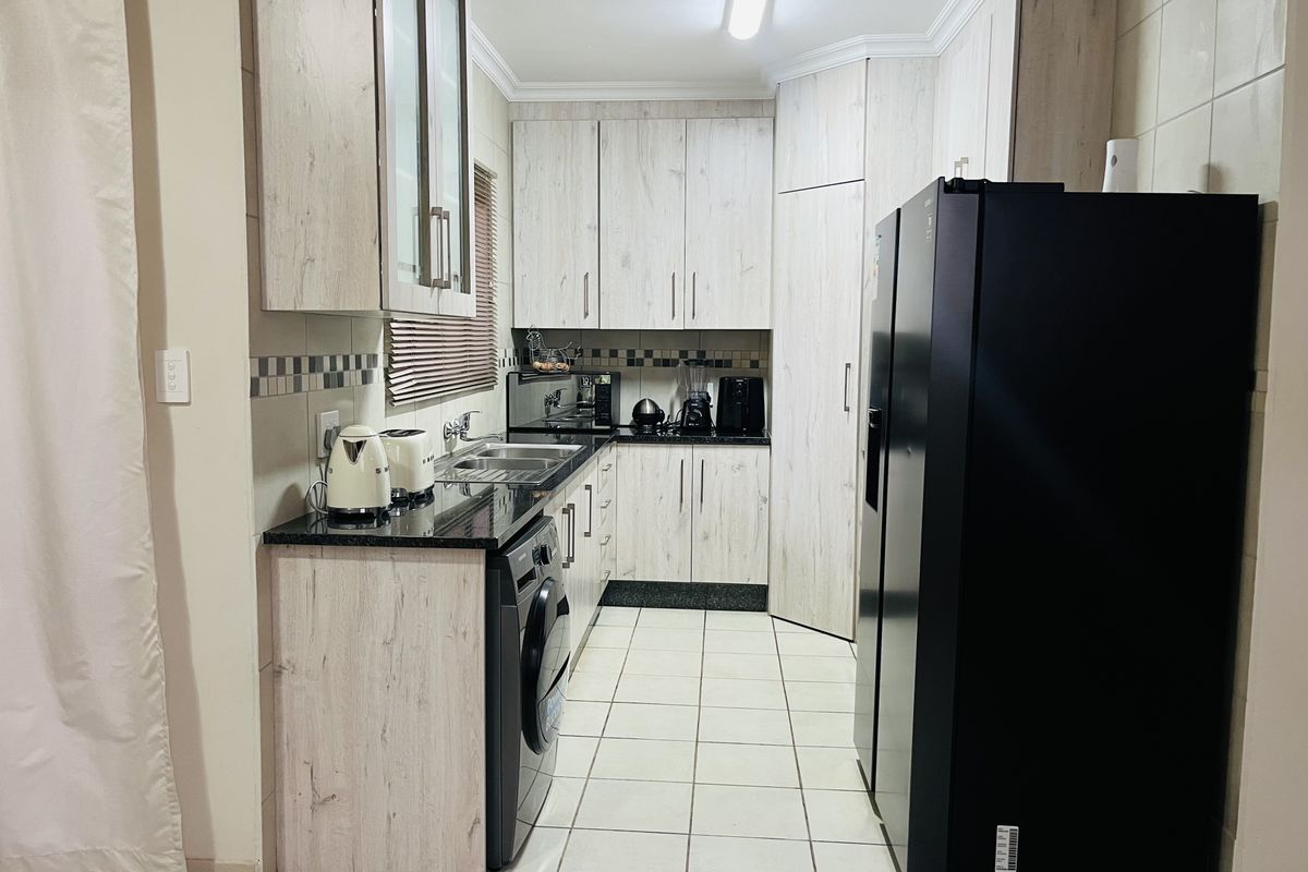 A functional kitchen featuring light wood-grain cabinetry, dark granite countertops, tiled flooring, and a dedicated space for laundry appliances.