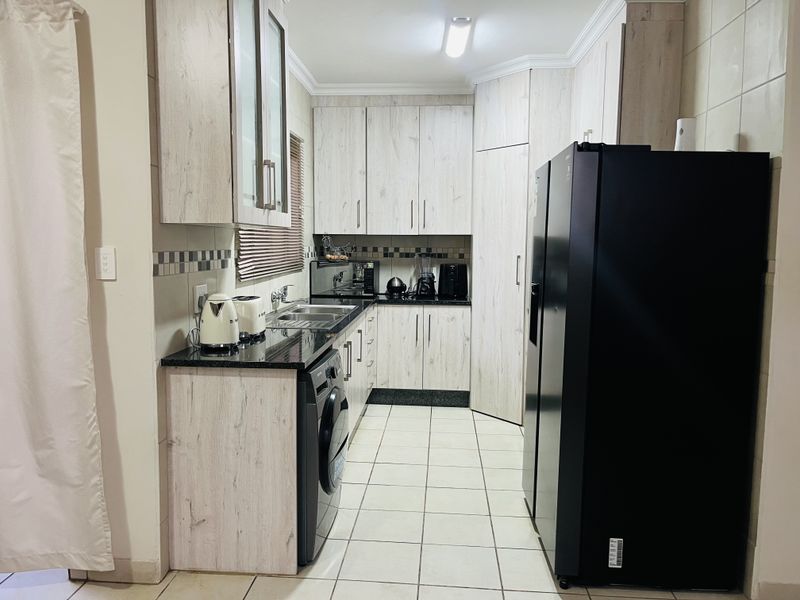 A functional kitchen featuring light wood-grain cabinetry, dark granite countertops, tiled flooring, and a dedicated space for laundry appliances.